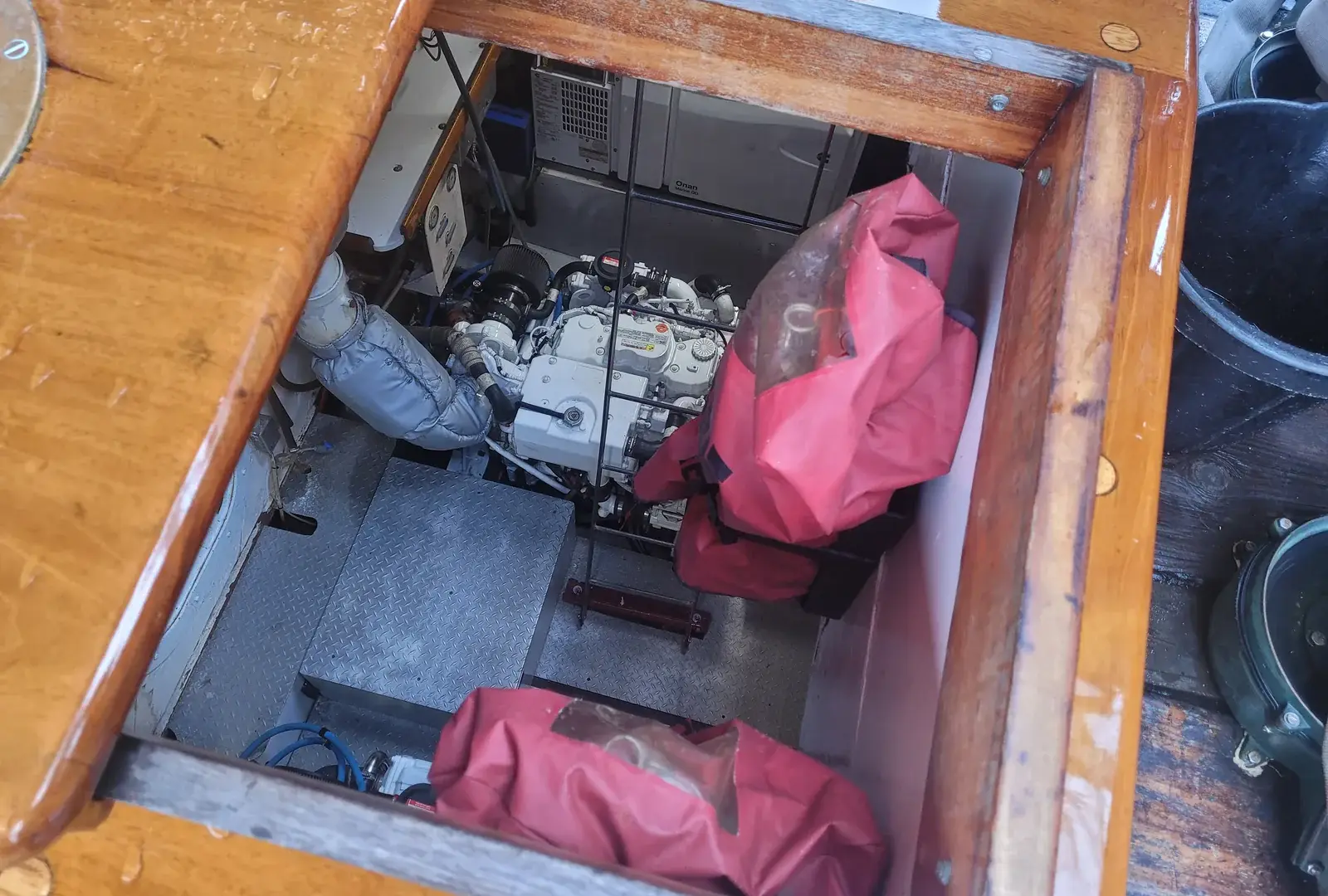 A marine diesel engine seen through an open timber hatch in the deck of a wooden sailing vessel